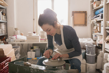 Caucasian woman is shaping pottery clay on a pottery wheel in a ceramic workshop.