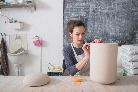 A ceremic artist is putting the finishing touches to a ceramic urn in a ceramic workshop.