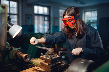 Young woman is practicing on shop floor lathe for college. Concept female profession carver for...