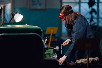 Young woman engineer behind stunt cnc in goggles stands in shop floor factory. Concept industrial procession.