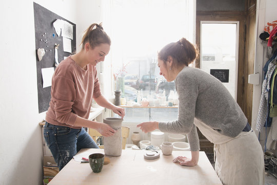 Two ceremic artists are putting the finishing touches to a ceramic pitcher in a pottery workshop.