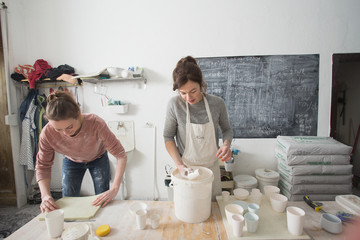 Two ceremic artists are glazing ceramics in a pottery workshop.