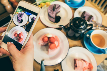 Desserts sweets table mobile food photo with cell phone. Cafe table top view. Cakes and tea time