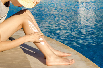 Young woman with sunscreen cosmetics products on leg holding sun protection cream bottle on the...