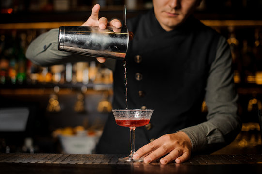 Barman pouring alcoholic drink with campari from shaker into the cocktail glass