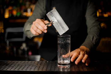 Barman putting a big rectangular piece of ice into a glass