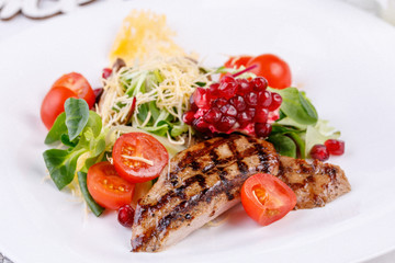 Appetizing pork steak with pomegranate decorated with cherry tomatoes and micro-green.