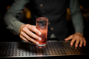 Barman hand holding a glass with summer light sour cocktail with pink peach liquor
