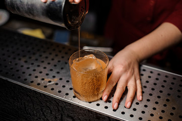 Female bartender hand pouring a fresh drink from shaker into a glass