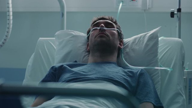 In the Hospital Sick Male Patient Sleeps on the Bed, He's Wearing Nasal Cannula to Help Him Breath. Terminally Ill Man in a Come.  Sad and Blue Scene. Shot on RED EPIC-W 8K Helium Cinema Camera.