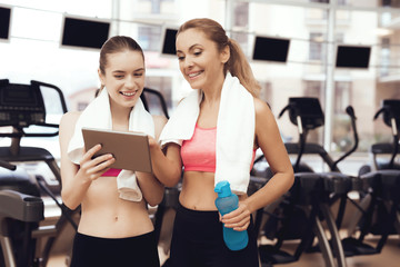 Mother and daughter using tablet at the gym. They look happy, fashionable and fit.