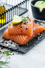 Two pieces of raw salmon fillet with fresh herb rosemary, spices and olive oil on black slate plate