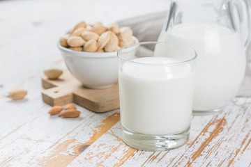 Almond milk in glass and jar on wood background