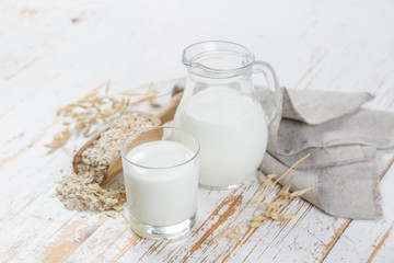 Oat milk in glass and jar on wood background
