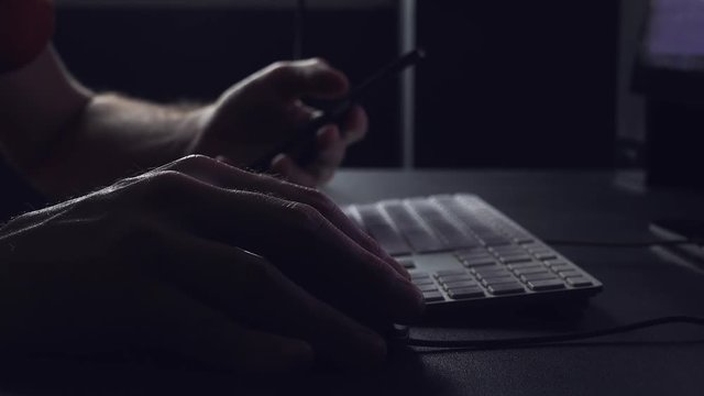 Freelancer using mobile phone and desktop computer ind ark office, low key footage