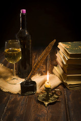 The concept of education and writing, an inkwell with a pen and a candle on the background of a roll of books and a bottle of wine with a glass