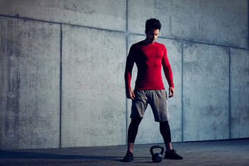 Handsome young man standing and looking down on kettlebell beofre exercise