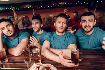 Sad blue team fans at bar in sports bar with red team fans cheering in background.