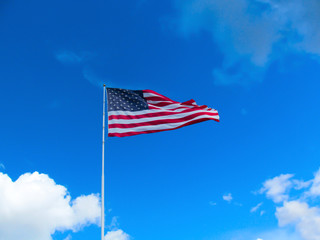 USA flag on the clear blue sky background.
Bright sunny view of a high flagpole with a flag in the wind.