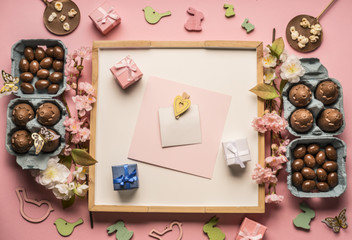 Easter composition with chocolate eggs, spring flowers,  various decorations, wooden rabbits and birds, small gifts on a pink background, space for text, top view