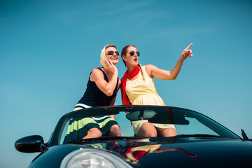 Woman having summer trip in convertible car stretching hands in the air with fun