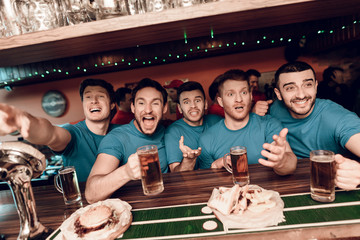 Blue team sports fans at bar drinking beer at sports bar with red team fans in background.