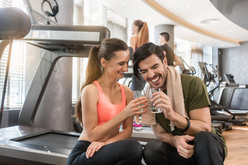 Cheerful young man and woman with a healthy lifestyle drinking plain water for hydration during break at the fitness club