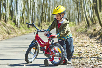 Fototapeta na wymiar Little child boy cycling on bicycle in green park outdoor in spring. A child is riding a children's bike with support training wheels wearing safety helmet 