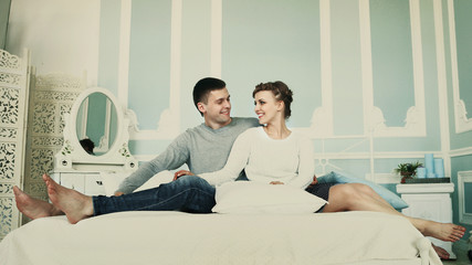 Young happy couple sitting in bed in spacious sleeping room