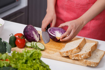 hand cutting purple cabbage on board in kitchen room