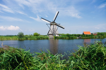 Naklejka premium Classic windmills by the canal in Dutch village Kinderdijk in Holland. Landscape of famous tourist destination in Europe.