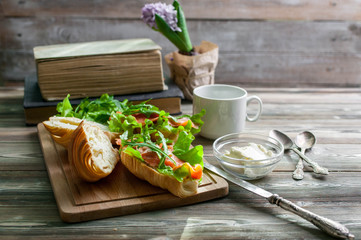 The fresh baked croissants with butter, a salty salmon and leaves of arugula on a chopping board on a wooden table. Breakfast concept