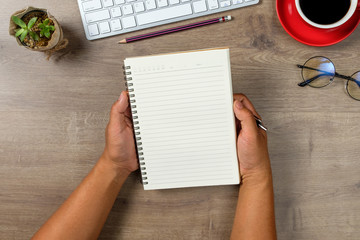 A man two hands hold the empty(blank) notebook isolated ,on desk office wooden top view