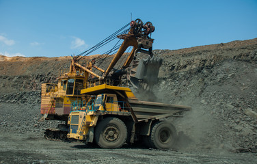 Obraz premium Excavator in the quarry loads the dumper with iron ore