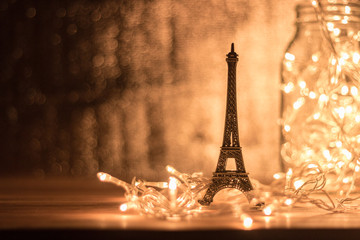The Eiffel model rests on a wooden desk. Garland light has a background and has a blurry background.