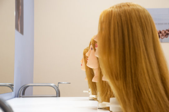 Three female heads of mannequins with long light straight blond hair stand in a row in perspective