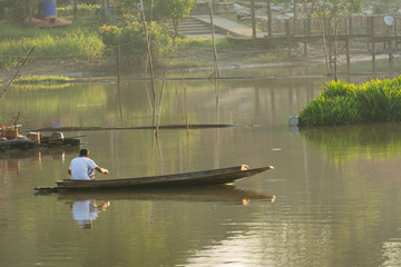 The old man fishing in the wooden boat in the early morning