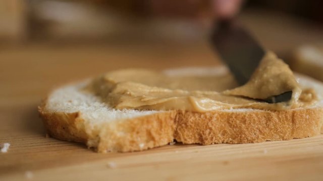 Delicious and hearty breakfast nut cream on a crisp bread. Man makes a peanut butter sandwich.. Closeup of male hands spreading butter on bread in kitchen,  slow motion.