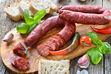 Spanische Spezialität: Luftgetrocknete scharfe Chorizo Paprikasalami auf Olivenholzbrett serviert – Spanish salami: Spicy chorizo sausage with tomatoes and basil served on an olive wood cutting board