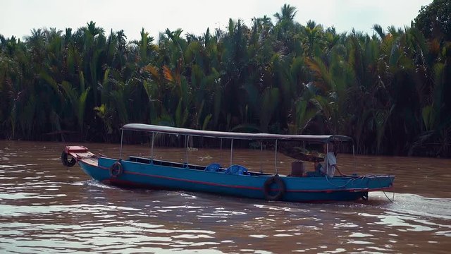 Fast shot following a man sailing a long boat down the Mekong River in Vietnam