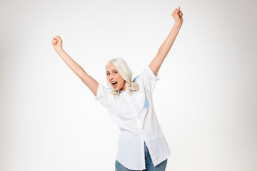 Photo of happy female pensioner 60s with gray hair raising her arms and screaming in delight, isolated over white background