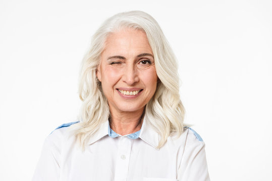 Portrait of adult gorgeous woman with gray hair winking and smiling with perfect teeth, isolated over white background