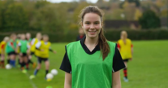 4K Portrait smiling girl, youth soccer player with teammates training in background