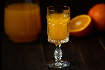 Fresh orange juice in crystal glass with fresh fruits on dark wood table