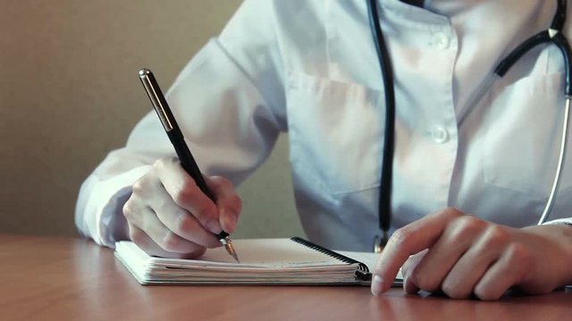 Female physician writes in notebook at the desc