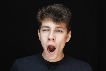 A teenager with a funny face yawns on a black background