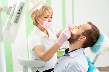 Obraz na płótnie Canvas Beautiful female dentist wearing pink mask is attending the teeth of a young male client of modern dentistry.