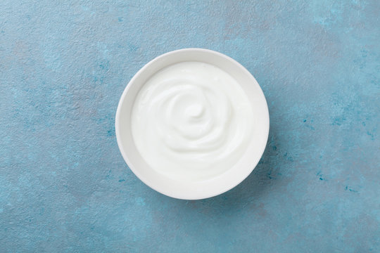 Greek yogurt in bowl on blue stone table top view.