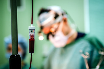 A dropper with donor blood in the operating room. In the background, an operating surgeon.
