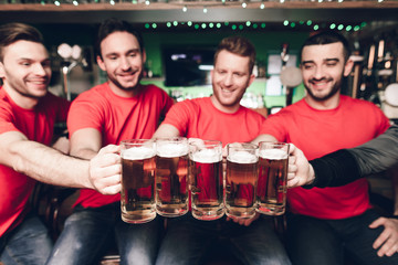 Five sports fans drinking beer cheering at sports bar.